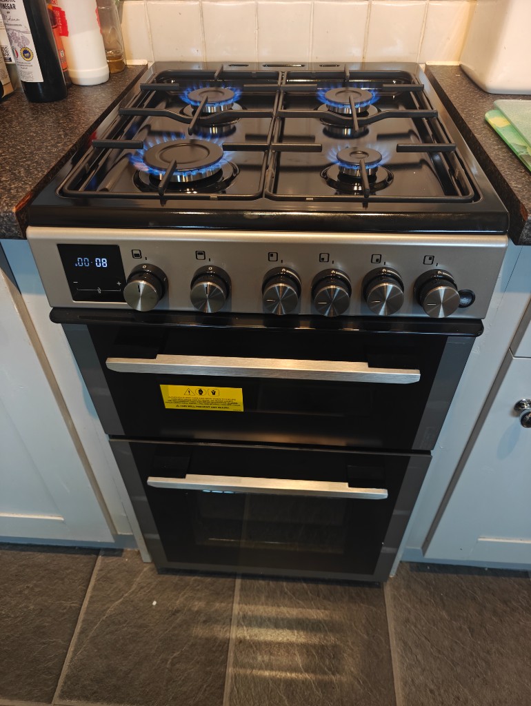 Freestanding gas cooker with four burners lit on the hob