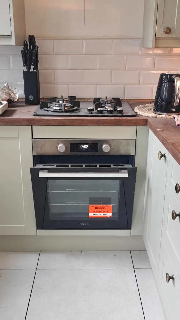 Built-in oven installed beneath a black glass gas hob with sage green cabinets